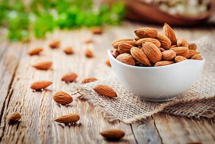 Almonds in white porcelain bowl on wooden table. Almond concept with copyspace.