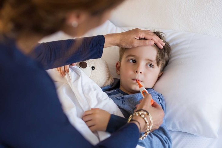 Sick boy with thermometer laying in bed and mother hand taking temperature. Mother checking temperature of her sick son who has thermometer in his mouth. Sick child with fever and illness in bed.