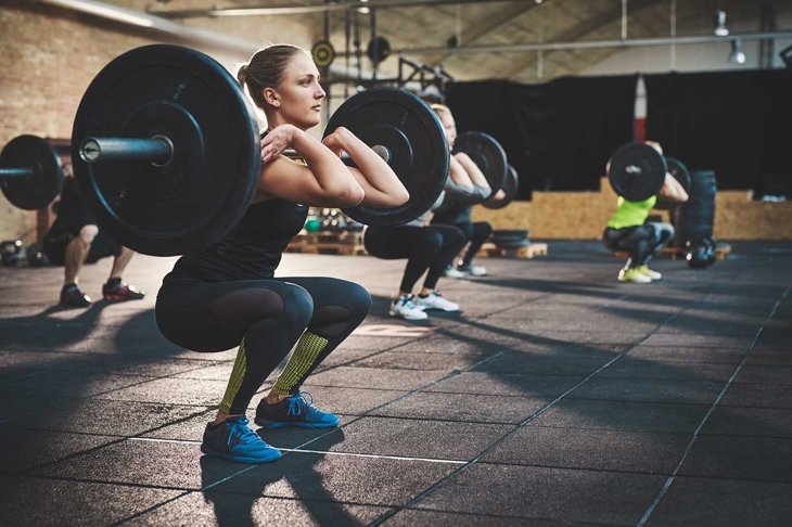 Fit young woman lifting barbells looking focused, working out in a gym with other people