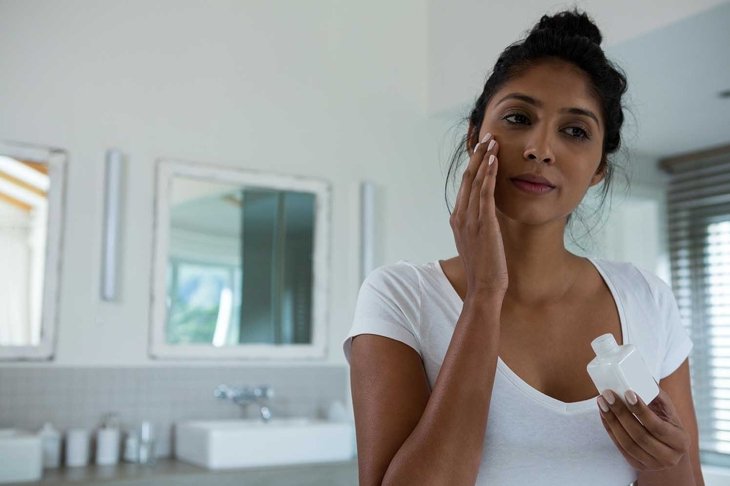 Close up of young woman applying lotion in bathroom at home