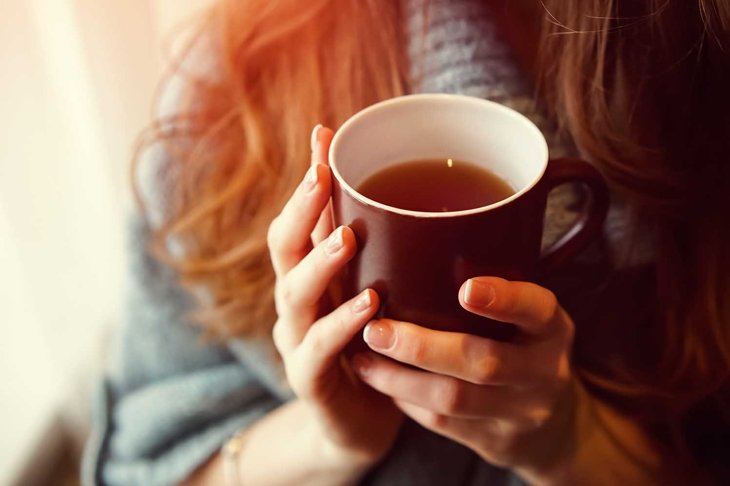 Drink Tea relax cosy photo with blurred background. Female hands holding mug of hot Tea in morning. Young woman relaxing tea cup on hand. Good morning Tea or Have a happy day message concept.