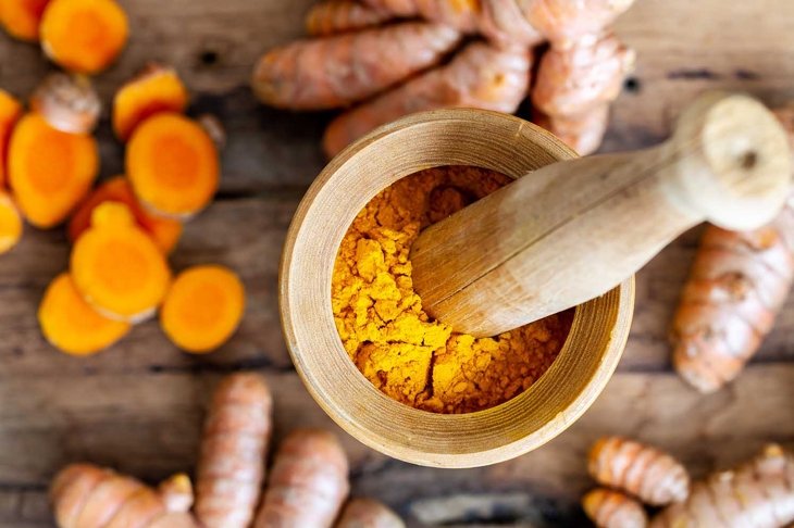 Turmeric powder in mortar with pestle, sliced curcumin, curcumin root on wooden background. Top view