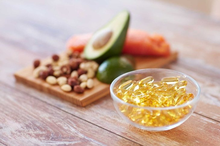 healthy eating, diet and omega 3 nutritional supplements concept - close up of cold liver oil capsules in glass bowl and food on table